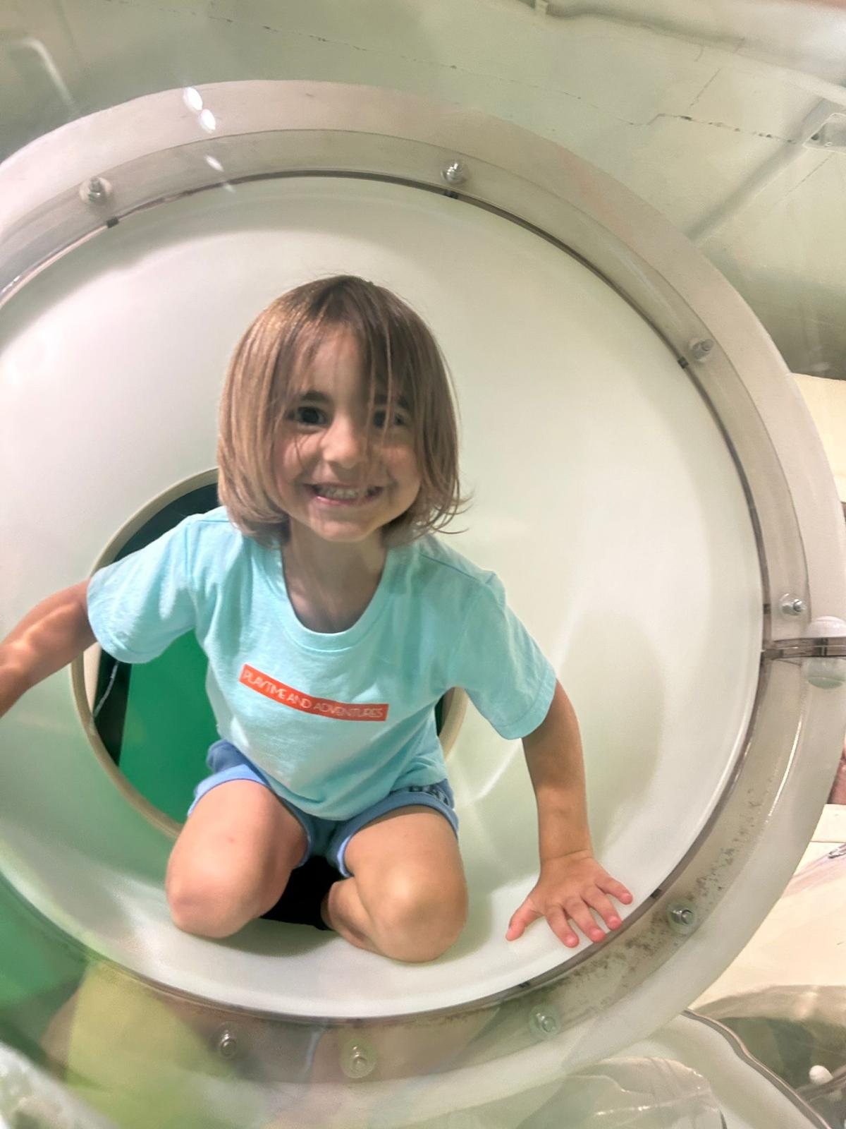A smiling child crawling through a play tunnel