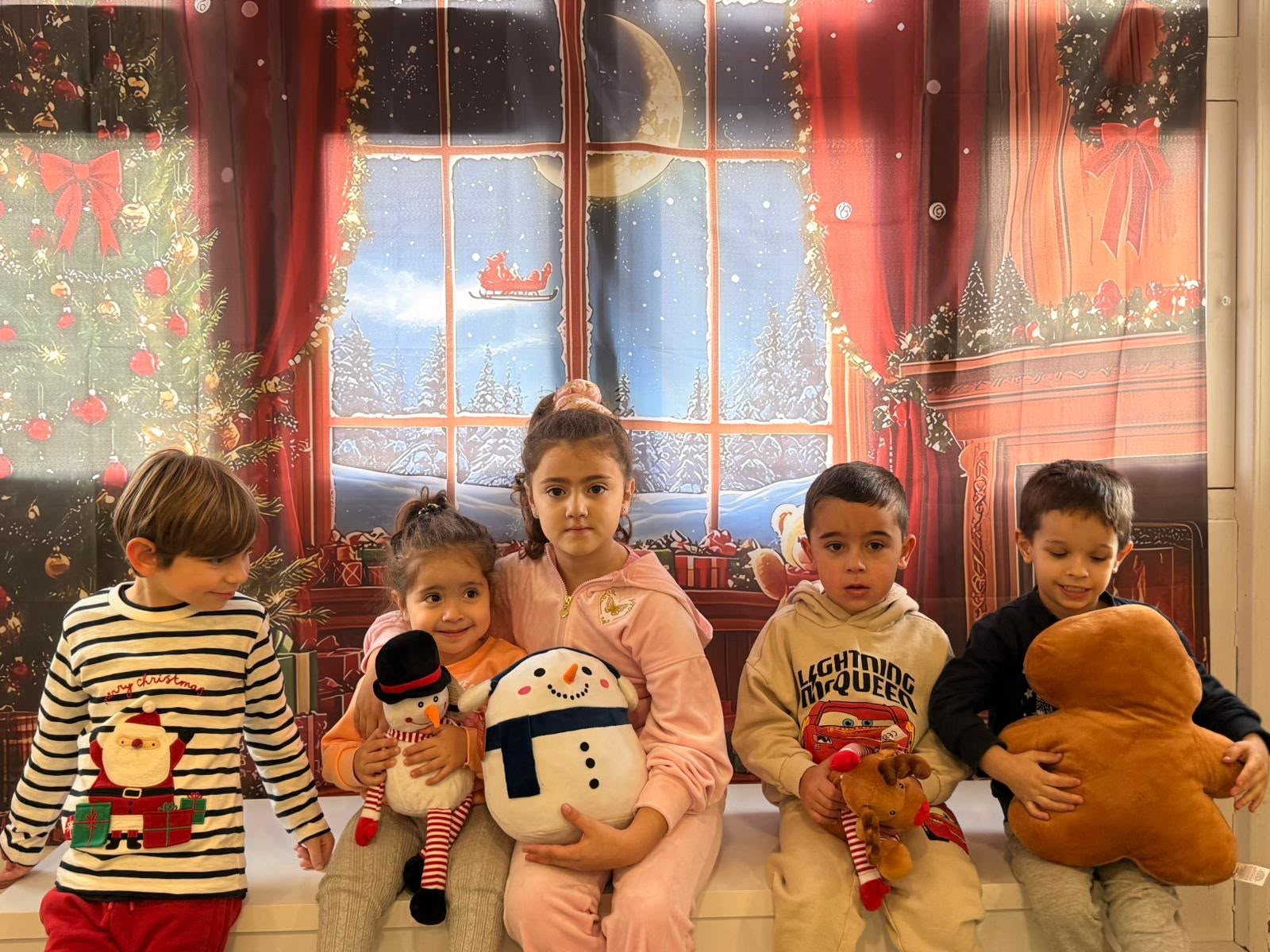 Children posing by a festive window display with a snowman
