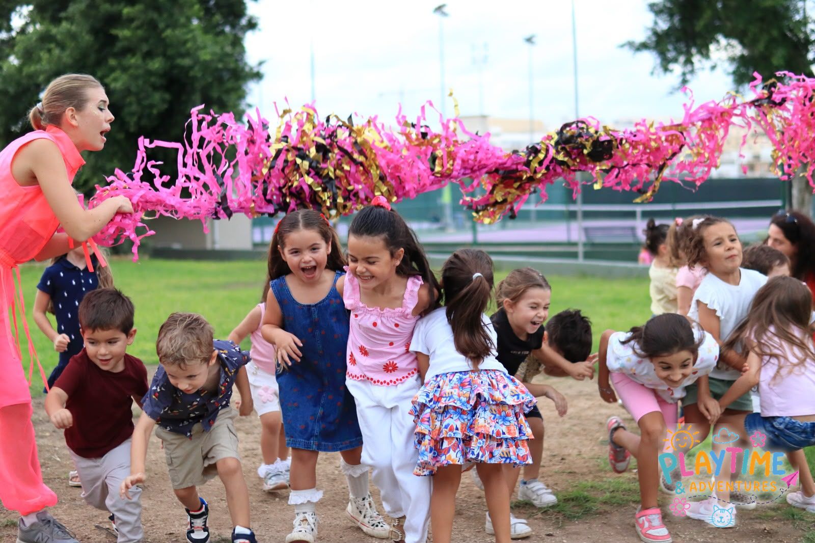 Children racing under a pink streamer, laughing