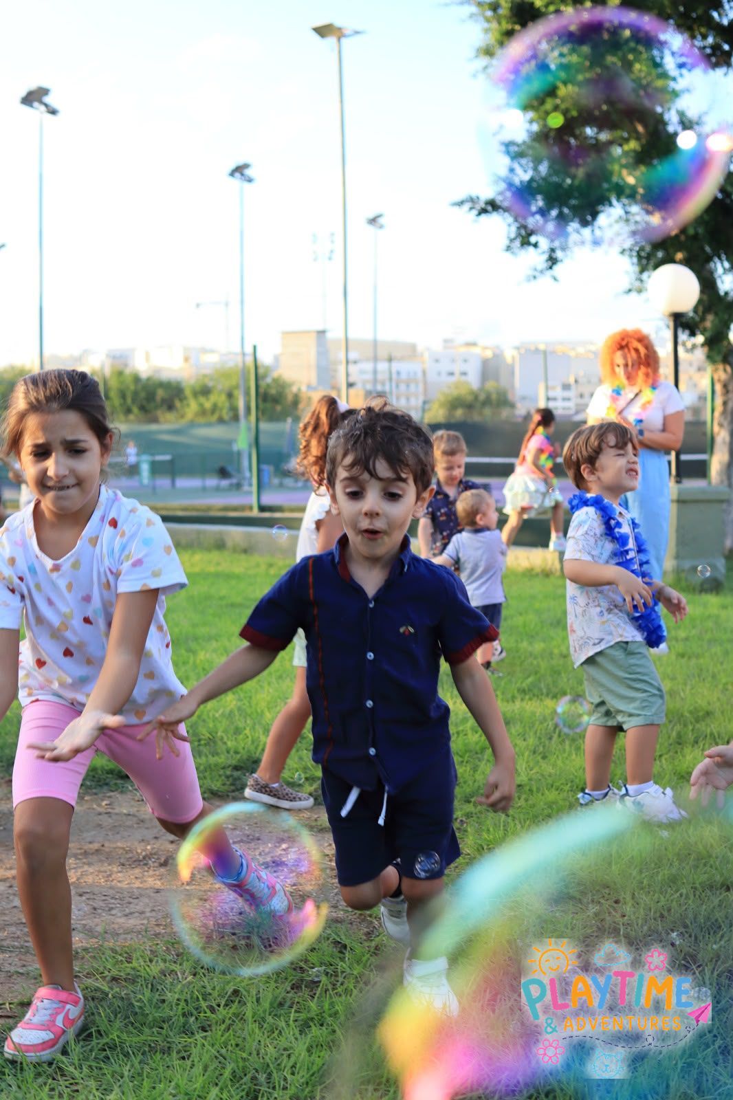 Children chasing giant bubbles on the grass